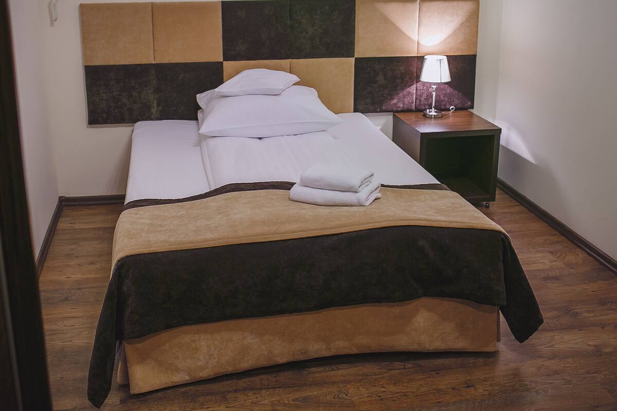A hotel room with a bed, a nightstand with a lamp, and a wall-mounted phone.
