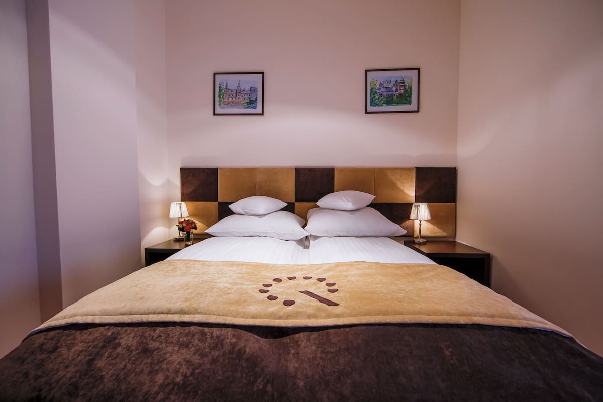 A neatly made bed with a patterned blanket, two bedside lamps, and two framed pictures on the wall.