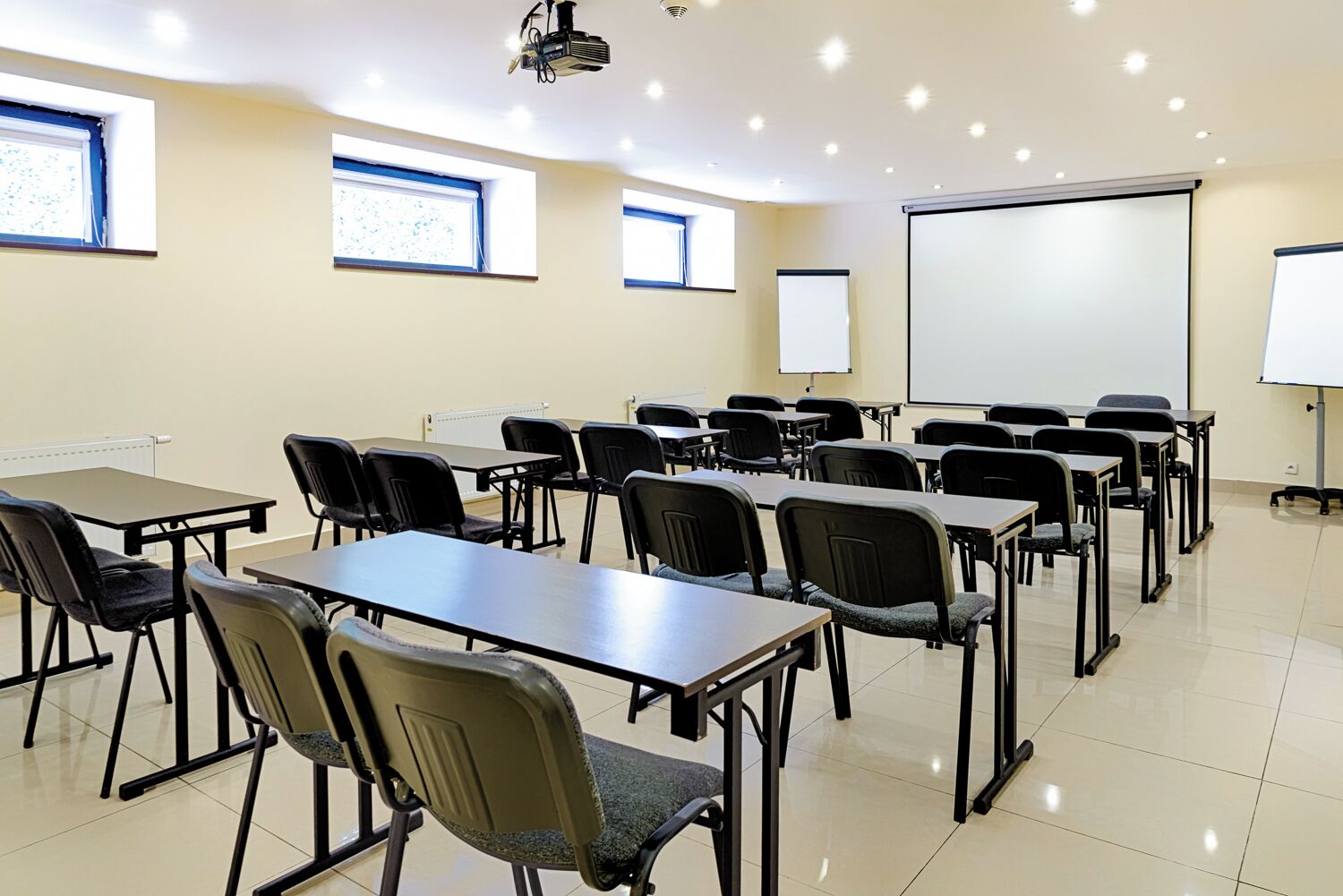 Un aula con filas de escritorios y sillas, un proyector y una pizarra.