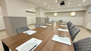 Un salón de conferencias con una larga mesa, sillas y un proyector.