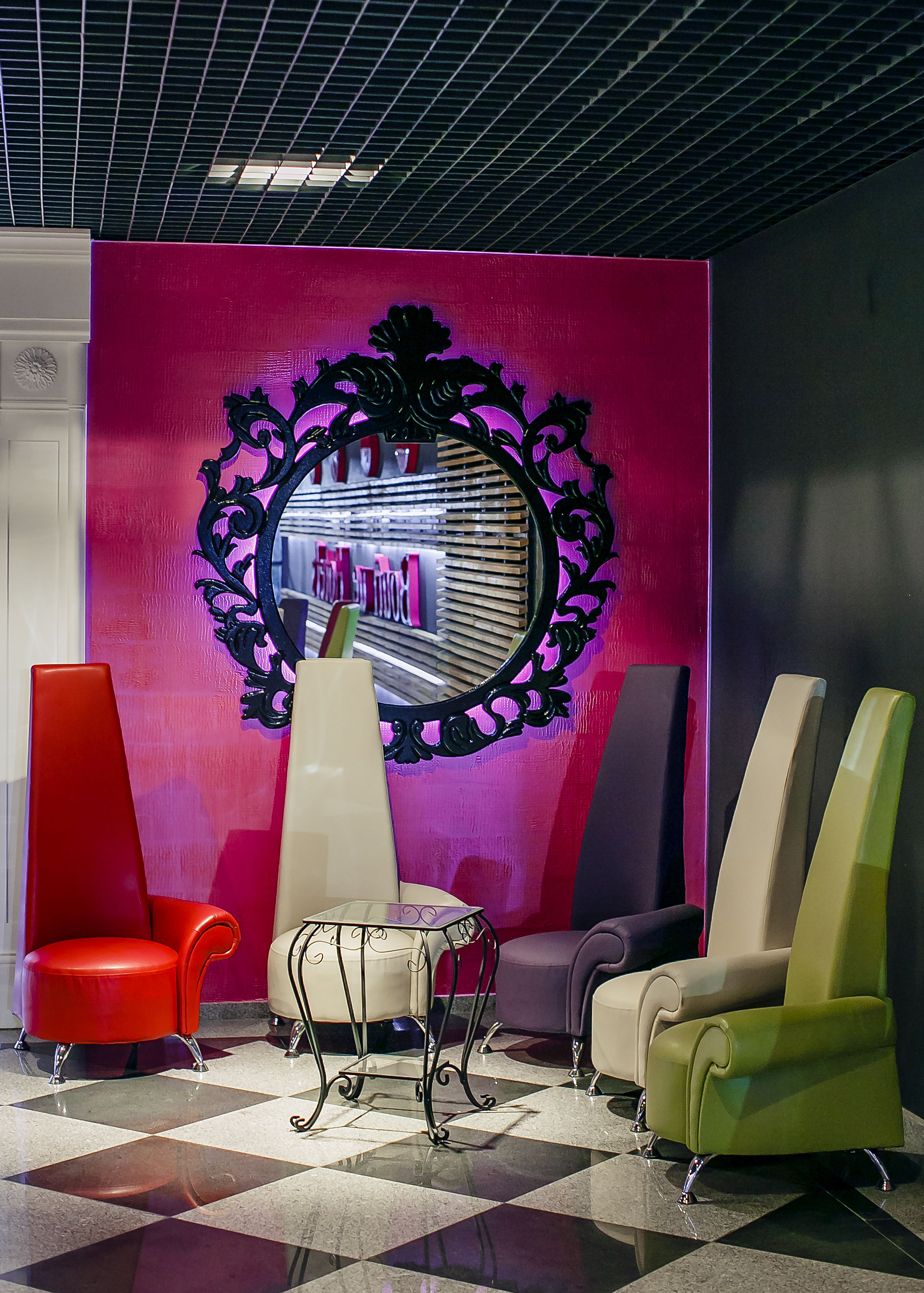 A lobby with a checkered floor, a central table, and three chairs in red, beige, and green.