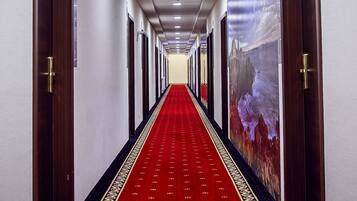 Ein Hotelgang mit rotem Teppich, Holztüren und einem Wandgemälde an der rechten Wand.