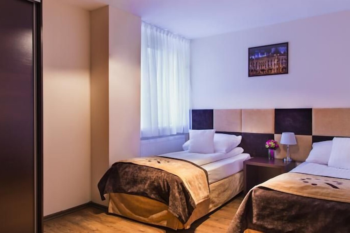 Habitación de hotel con dos camas, una mesita de noche, una lámpara y un cuadro en la pared.