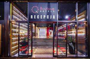The entrance of Boutique Hotel's reception area with a modern design, including a glass door, a signboard, and a staircase leading inside.