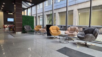 A modern lobby with a green wall, multiple seating areas, and large windows.