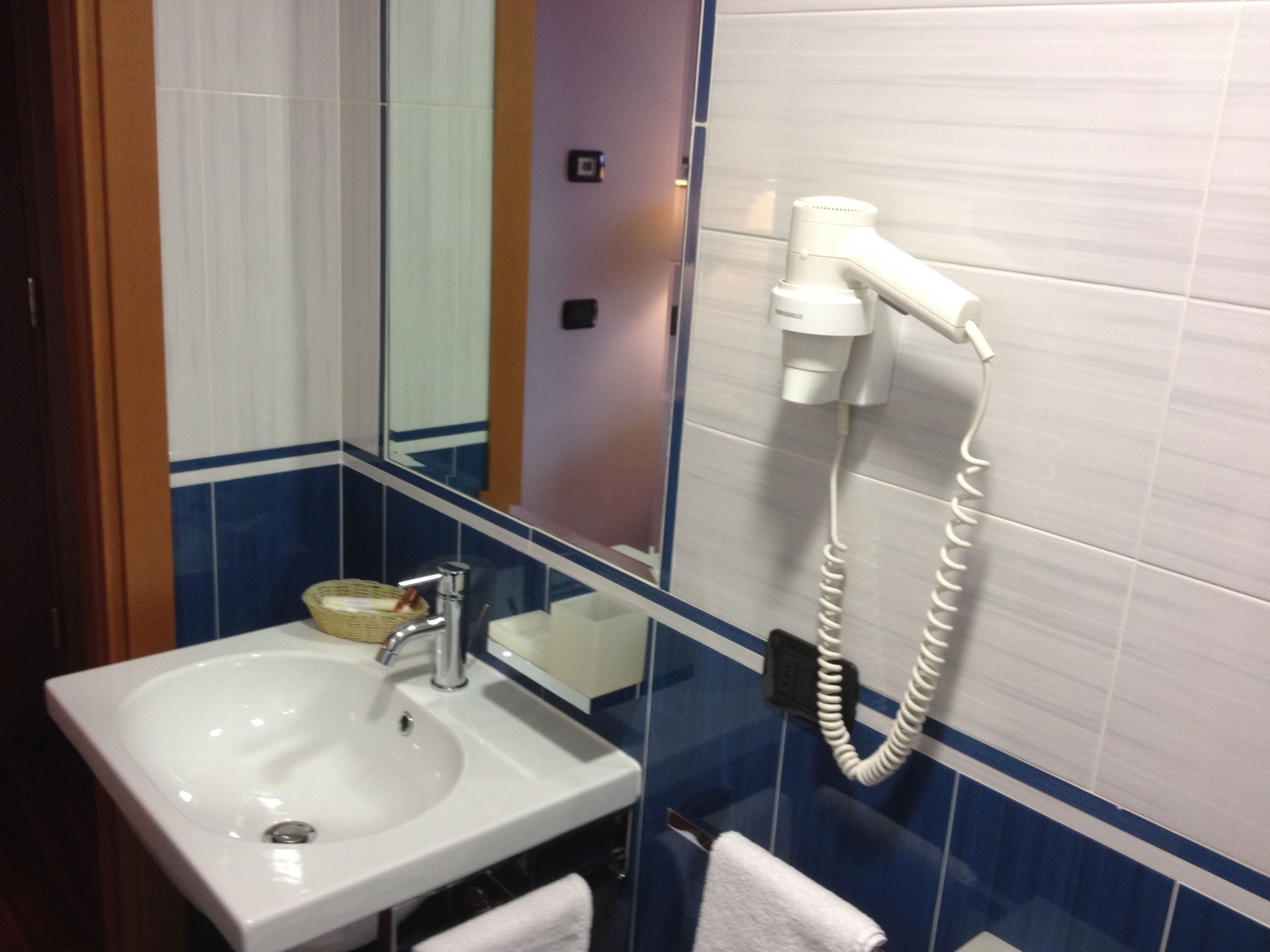 Un baño con un lavamanos blanco, un espejo y un secador de pelo montado en la pared.