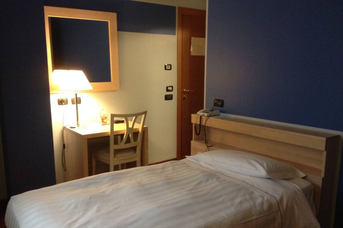Une chambre d’hôtel équipée d’un lit, d’un bureau, d’une chaise, d’une lampe et d’un téléphone.
