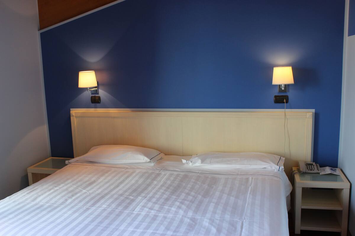 Une chambre d’hôtel comprenant un lit, deux tables de chevet et deux lampes fixées au mur.