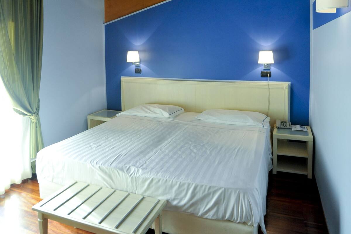 Une chambre avec un plafond en bois, un lit avec une literie blanche, deux lampes de chevet et une table de chevet.
