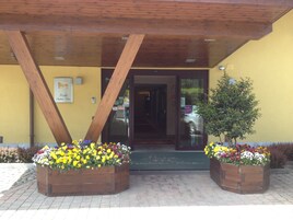 Entrada de edificio con vigas de madera, pared amarilla y macetas con flores.