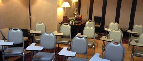 Un salón de conferencias con filas de sillas y mesas, equipado con lámparas y un jarrón decorativo.