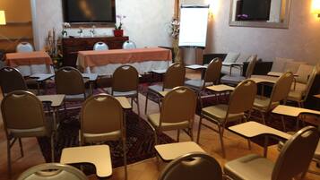 Un salón de conferencias con varias mesas y sillas, una televisión y una pantalla de proyector.