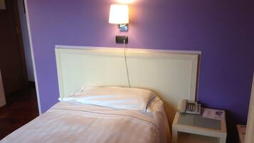 Habitación de hotel con una cama, una mesita de noche con un teléfono y una lámpara fijada a la pared.