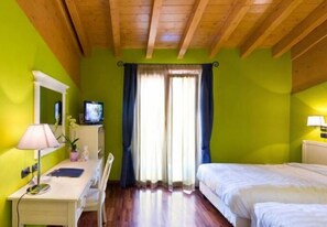Une chambre avec un lit, un bureau avec une lampe, une télévision et une fenêtre avec des rideaux.