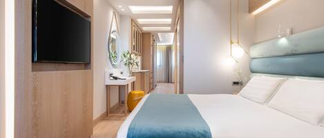 Habitación de hotel moderna con una cama grande, un televisor de pantalla plana montado en la pared, una mesita de noche con lámpara y vistas al pasillo.