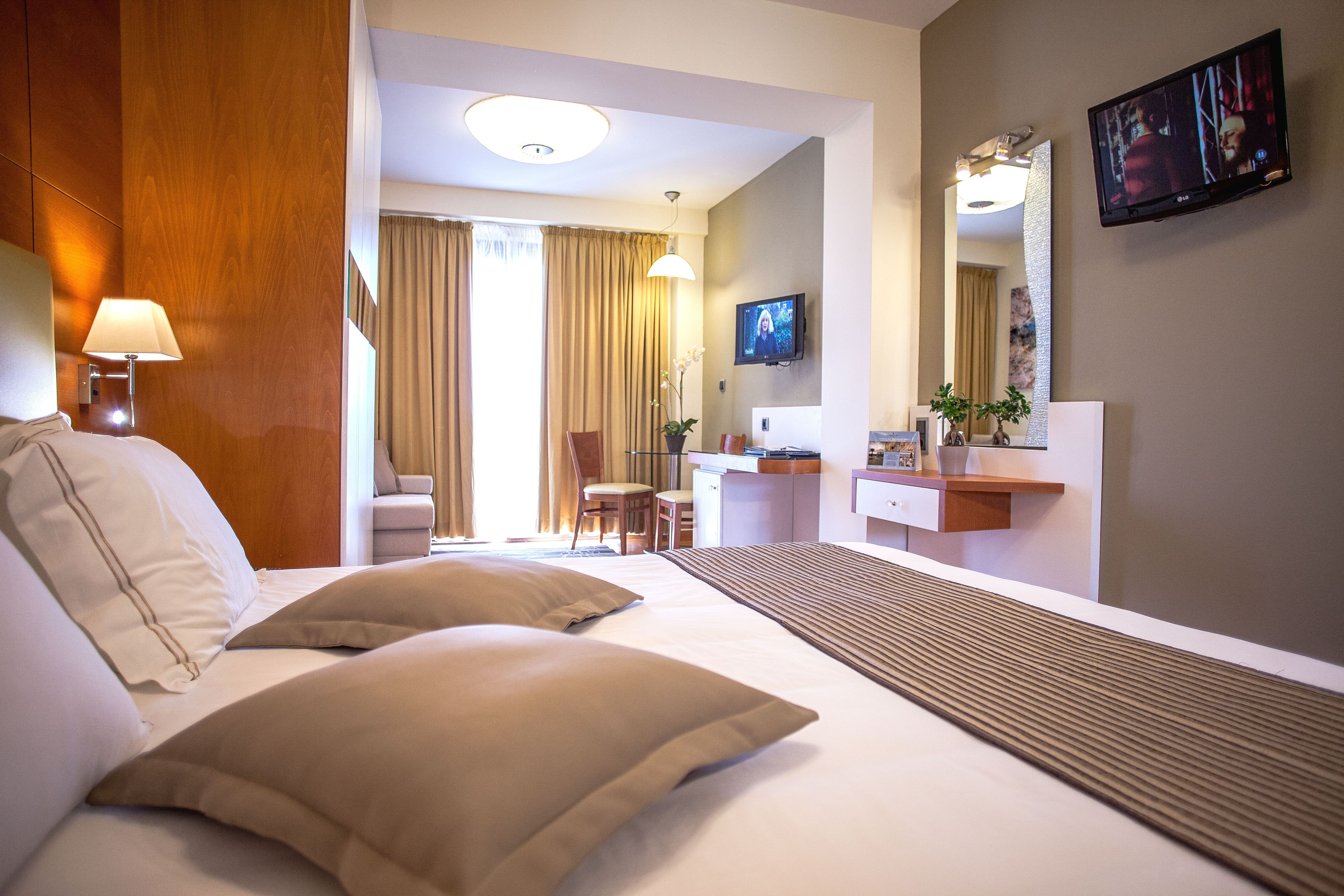 A hotel room with a bed, a desk, a chair, a television, and a mirror.