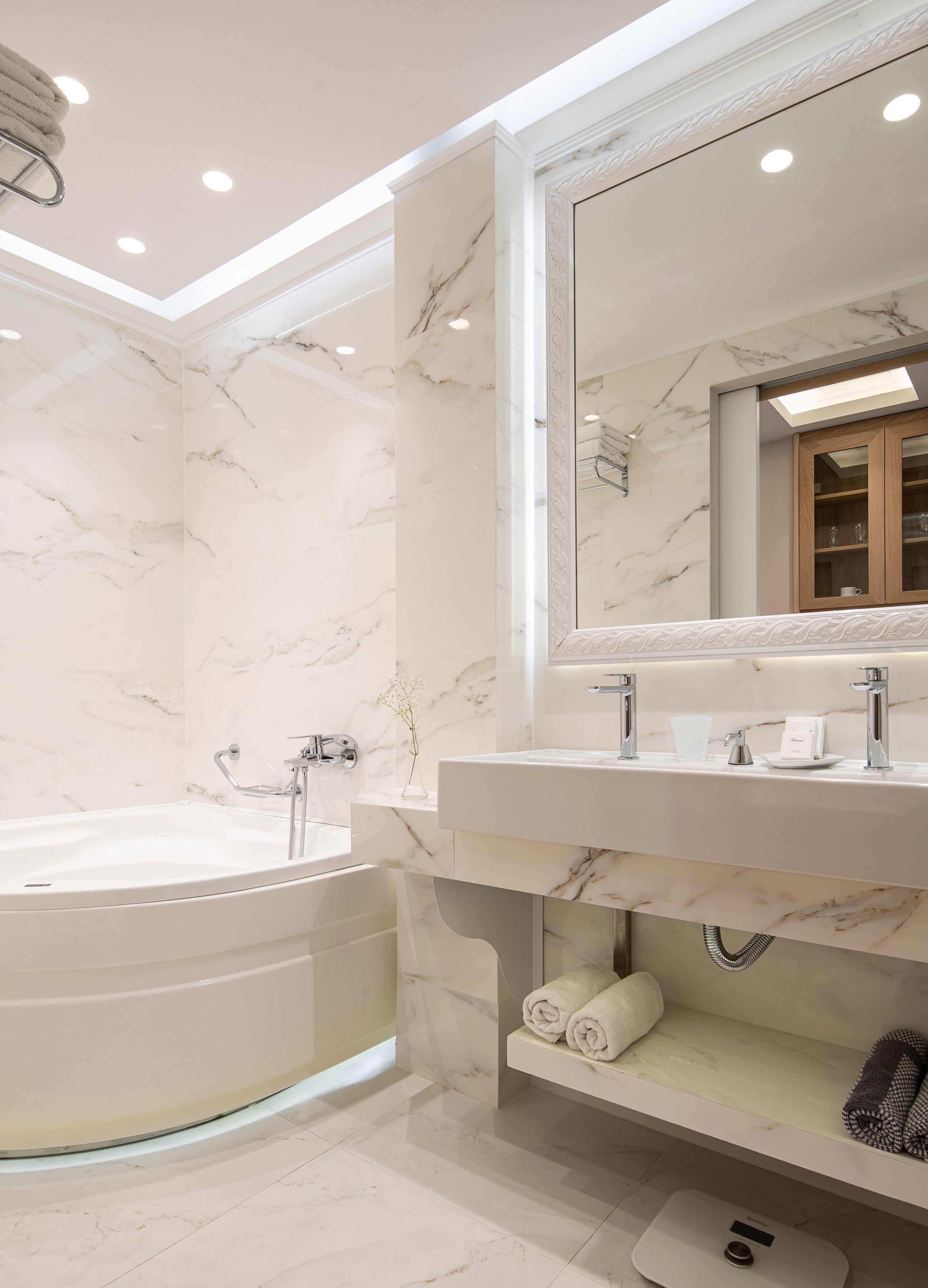 Une salle de bain moderne avec un mur en marbre, un grand miroir, une baignoire et un meuble-lavabo doté d’un évier et d’un porte-serviettes.