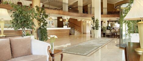 A spacious lobby with a high ceiling, a reception desk, a sofa, a coffee table, and a staircase leading to an upper level.