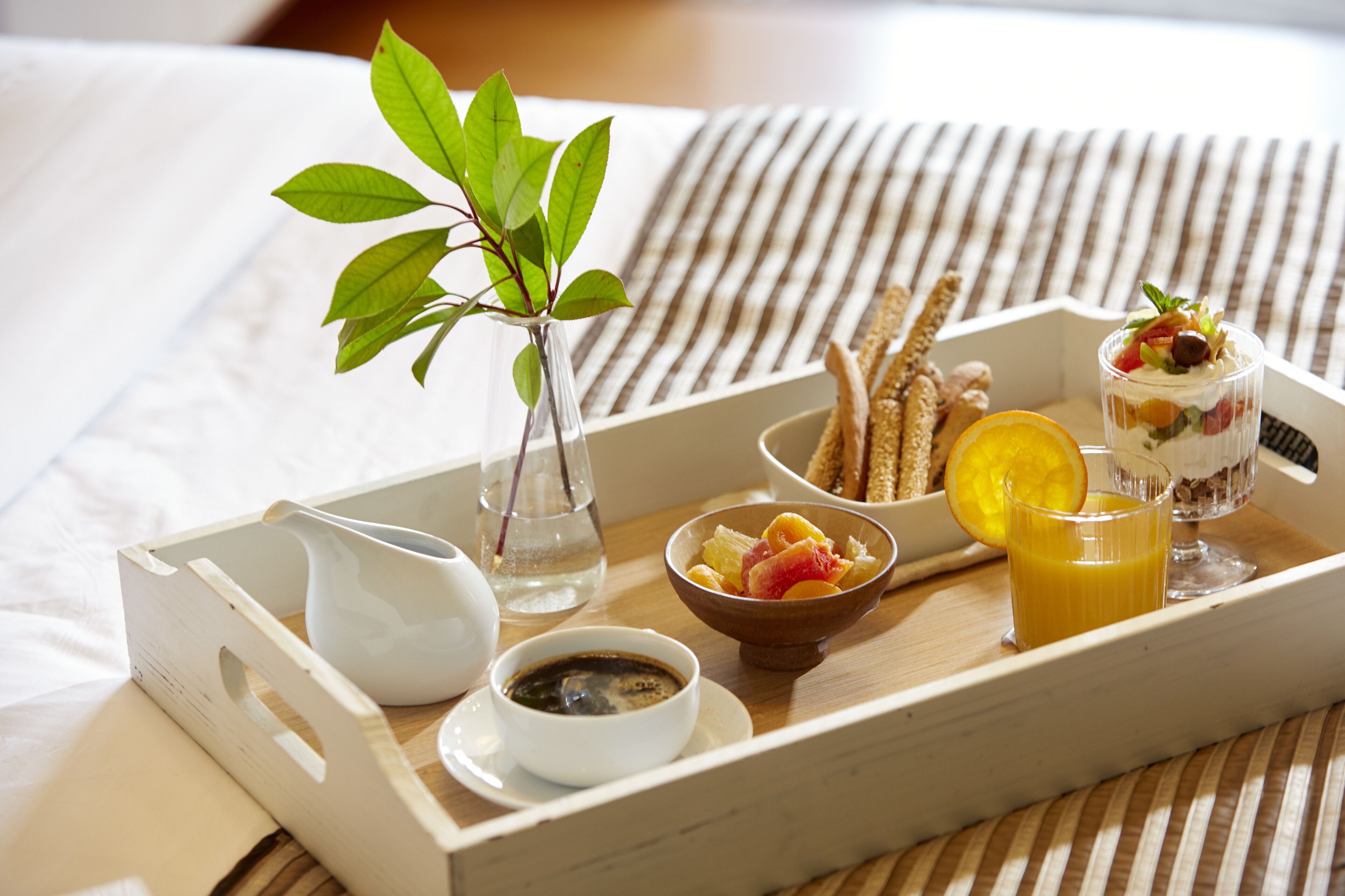 A tray with breakfast items including a bowl of fruit, a glass of orange juice, a cup of coffee, and a small vase with a plant.
