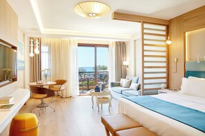 A hotel room with a bed, a sofa, a desk with chairs, a small table, and a balcony with a view. - Anthemus Sea Beach Hotel & Spa (Sithonia)