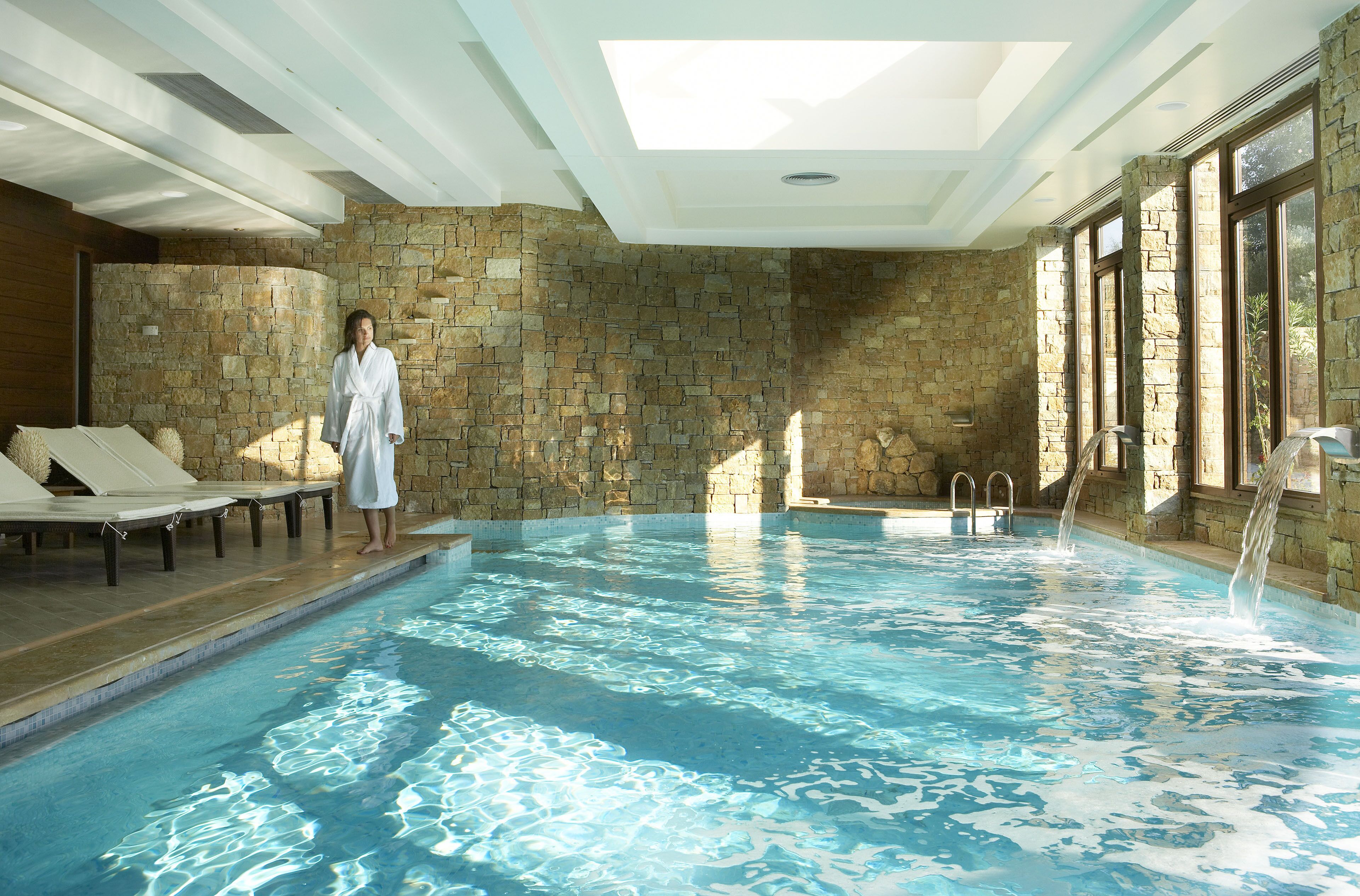 A large indoor swimming pool with stone walls and a skylight.