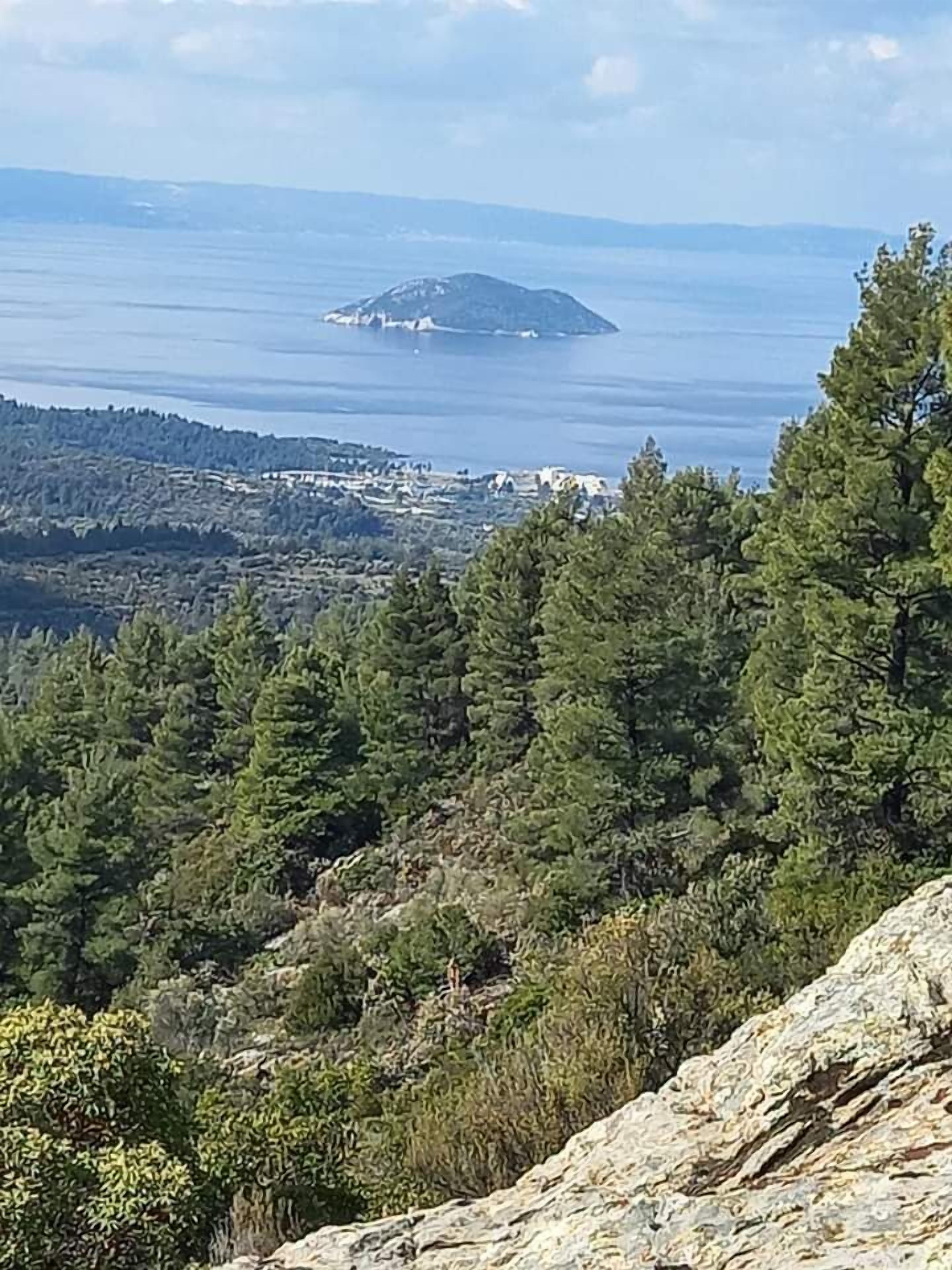 Un paysage montagneux, avec de vastes forêts et une vue sur une île lointaine.