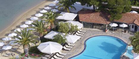 Eine Luftaufnahme eines Resorts mit Schwimmbad, Liegestühlen am Strand und Sonnenschirmen.