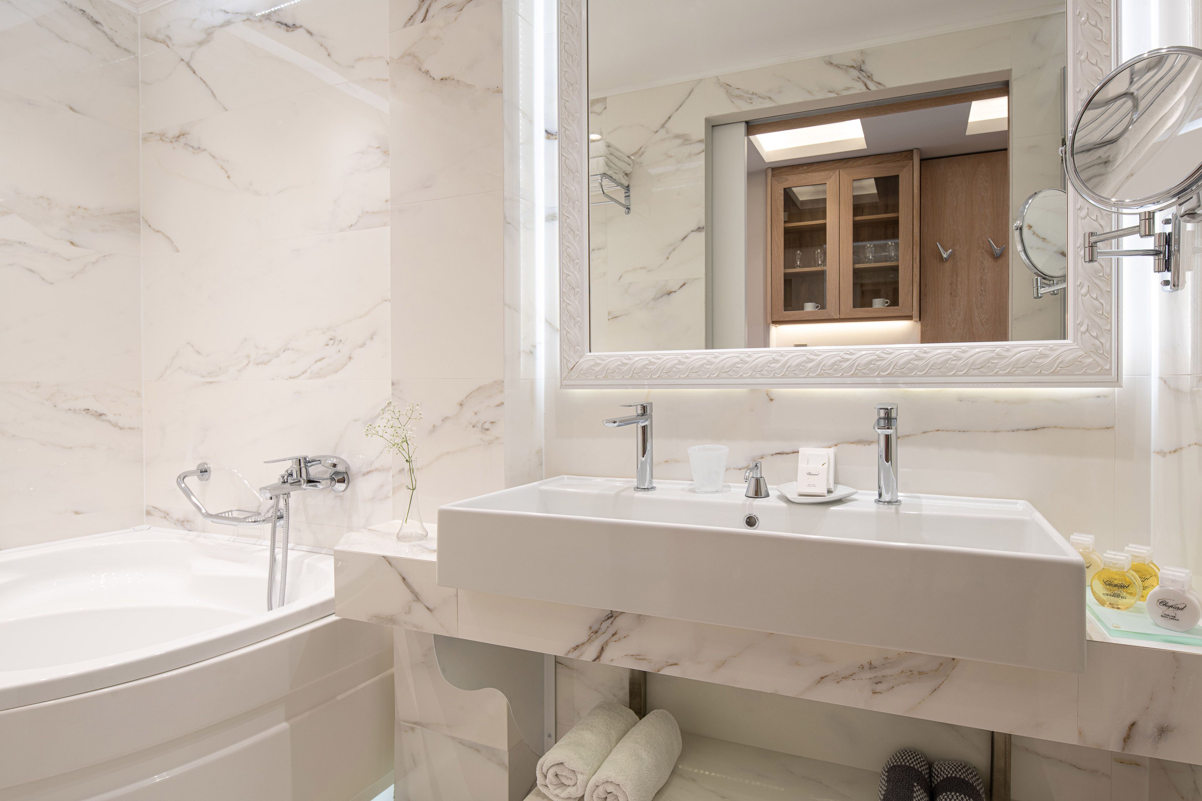 A bathroom with a marble sink, a bathtub, and a large mirror.