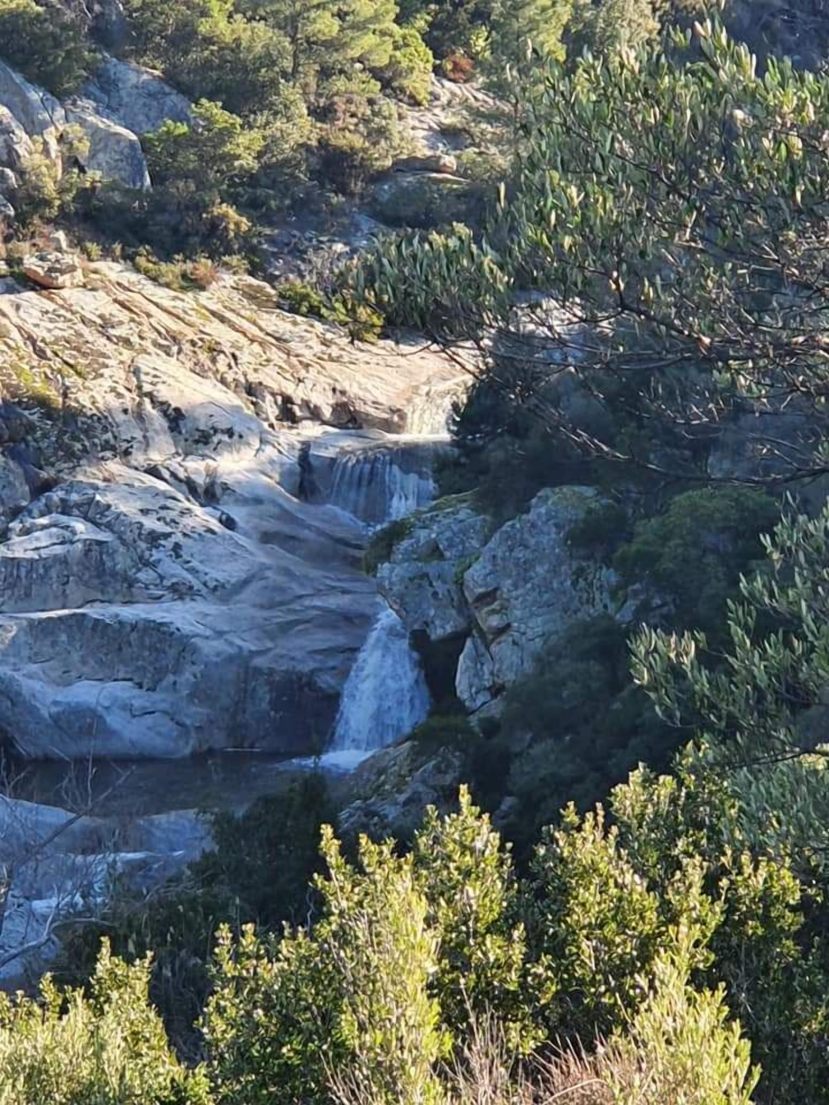 A natural landscape with a waterfall cascading over rocky terrain, surrounded by dense greenery.