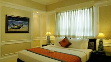 A hotel room with a large bed, two bedside tables, a nightstand, a window with curtains, a painting on the wall, and a lamp on each bedside table.