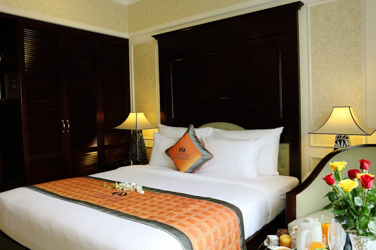 A hotel room with a large bed, two bedside lamps, a nightstand with a vase of flowers, and a tray with breakfast items.