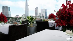 Un espace de restauration aménagé sur le toit, offrant une vue panoramique sur la ville, avec une table, des chaises et des plantes en pot.