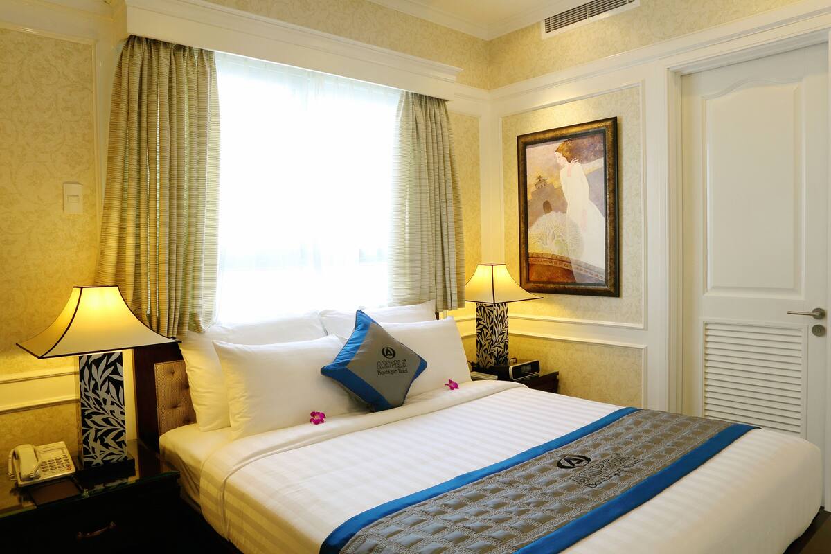 A hotel room with a neatly made bed, two bedside lamps, a telephone, and a painting on the wall.
