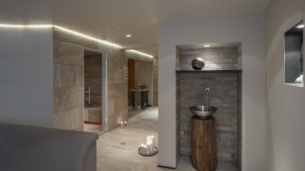 A modern bathroom with a stone wall, a sink, and a wooden stool. - Boutique Hotel St. Georg (Einsiedeln)