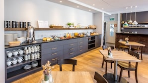 A modern kitchen with a central island, built-in shelves, and a dining area with wooden tables and chairs. - Boutique Hotel St. Georg (Einsiedeln)