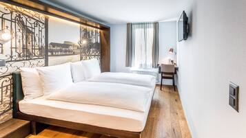 A hotel room with a large bed, a desk, a chair, a TV, and a view of a building through a decorative metal partition.