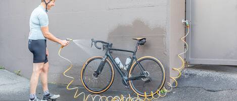Una persona lava una bicicleta con una manguera cerca de una pared.