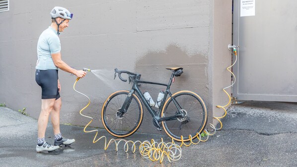 A person cleaning a bicycle with a hose against a wall.