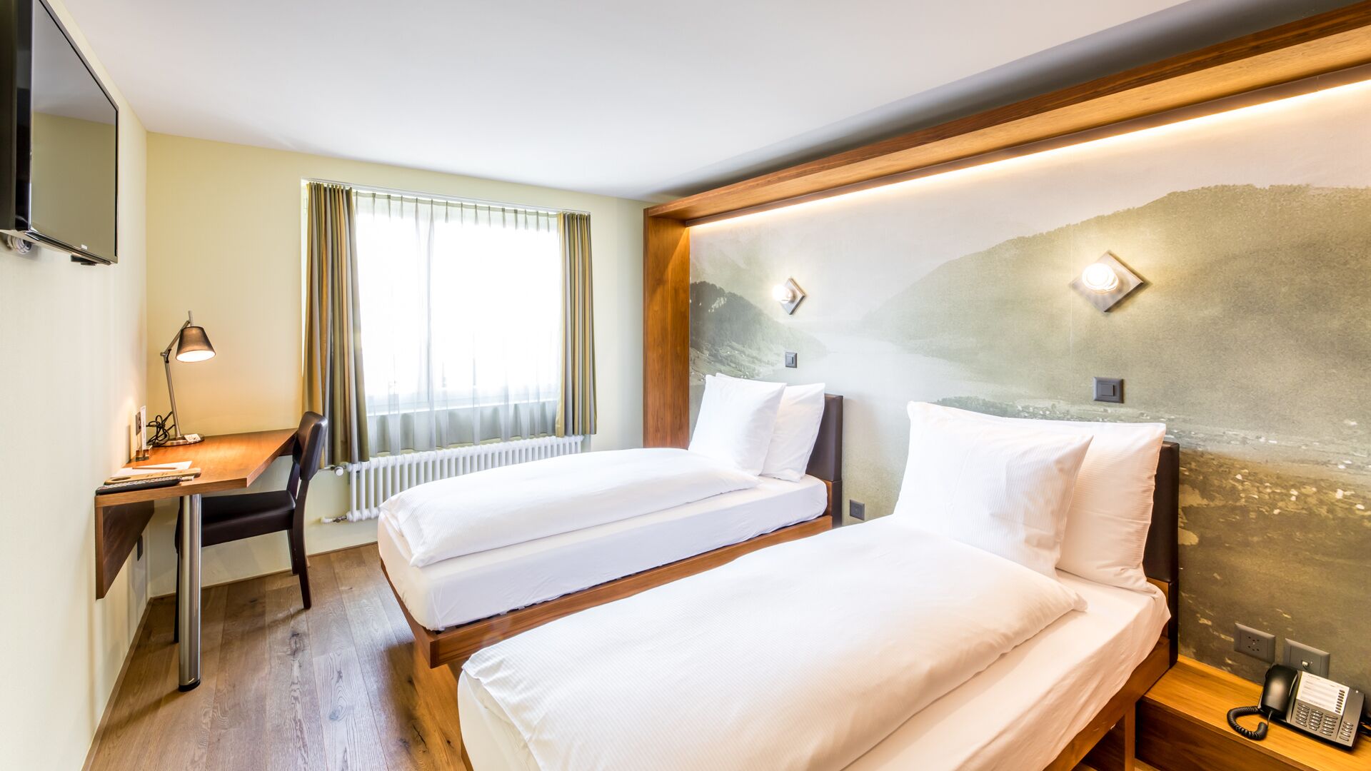 Une chambre d’hôtel avec deux lits, un bureau, une chaise, une télévision et un téléphone sur la table de chevet.