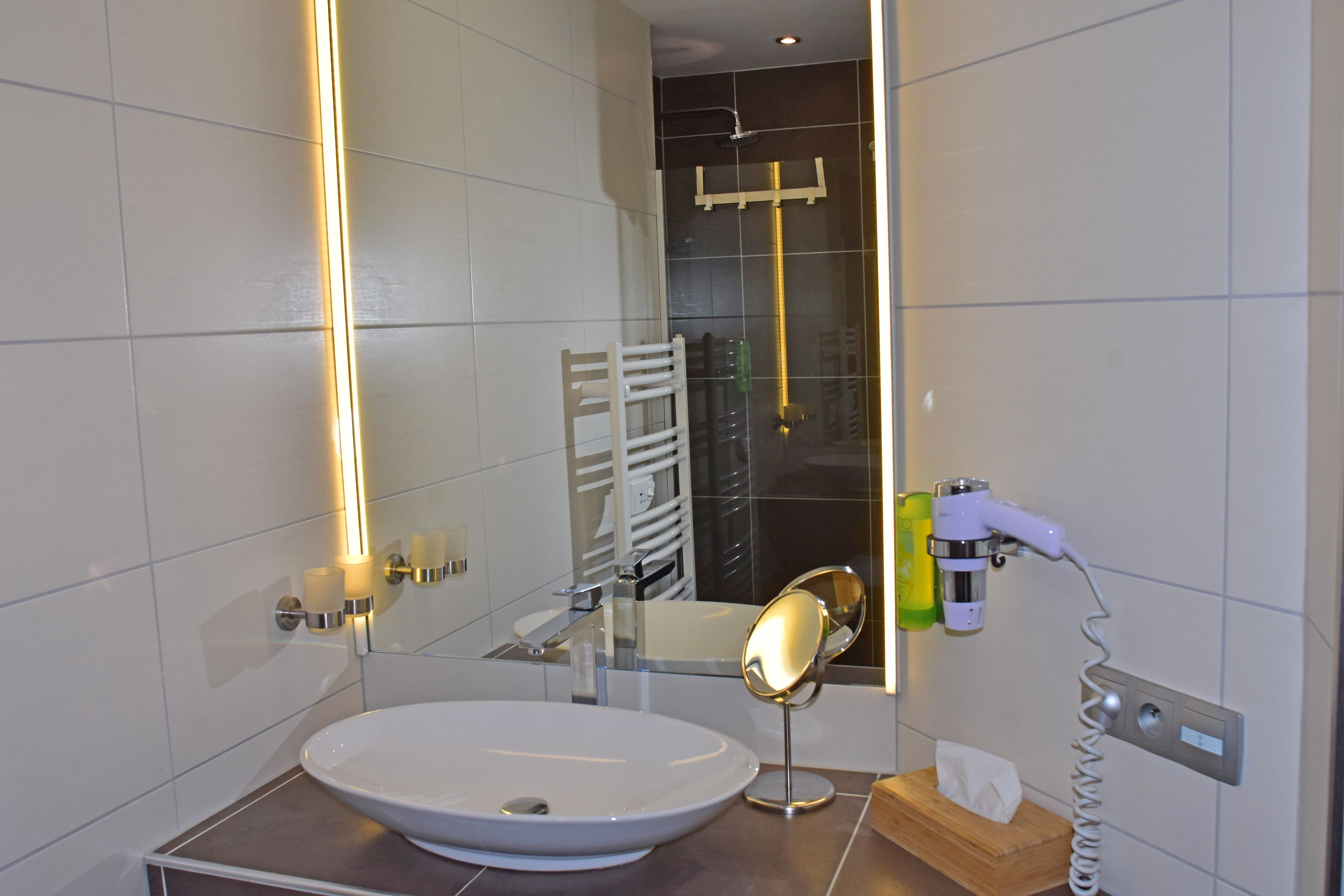 Un bany modern amb un gran mirall, un lavabo i una dutxera.