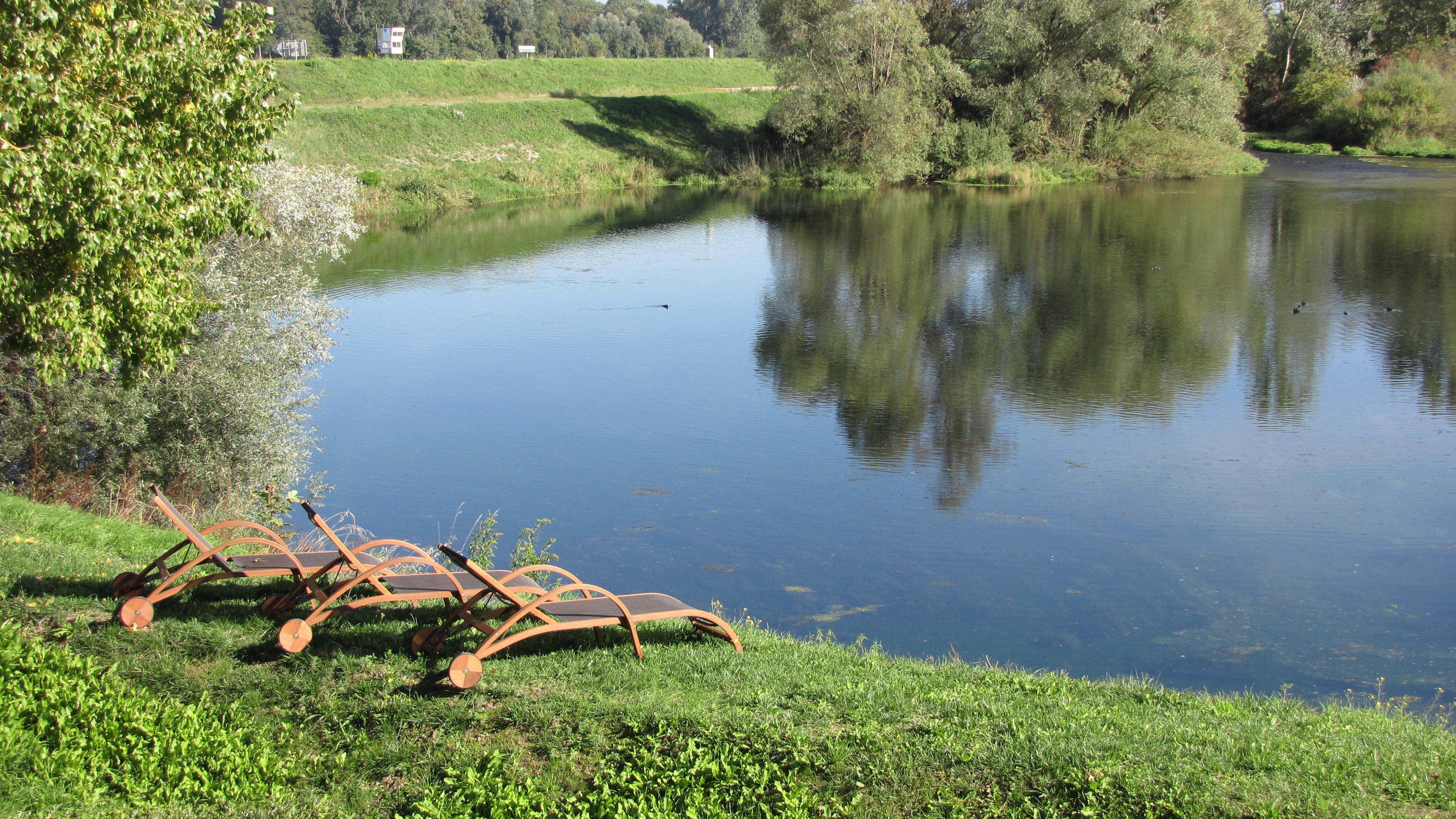 A serene lakeside setting with a grassy area and a few lounge chairs.