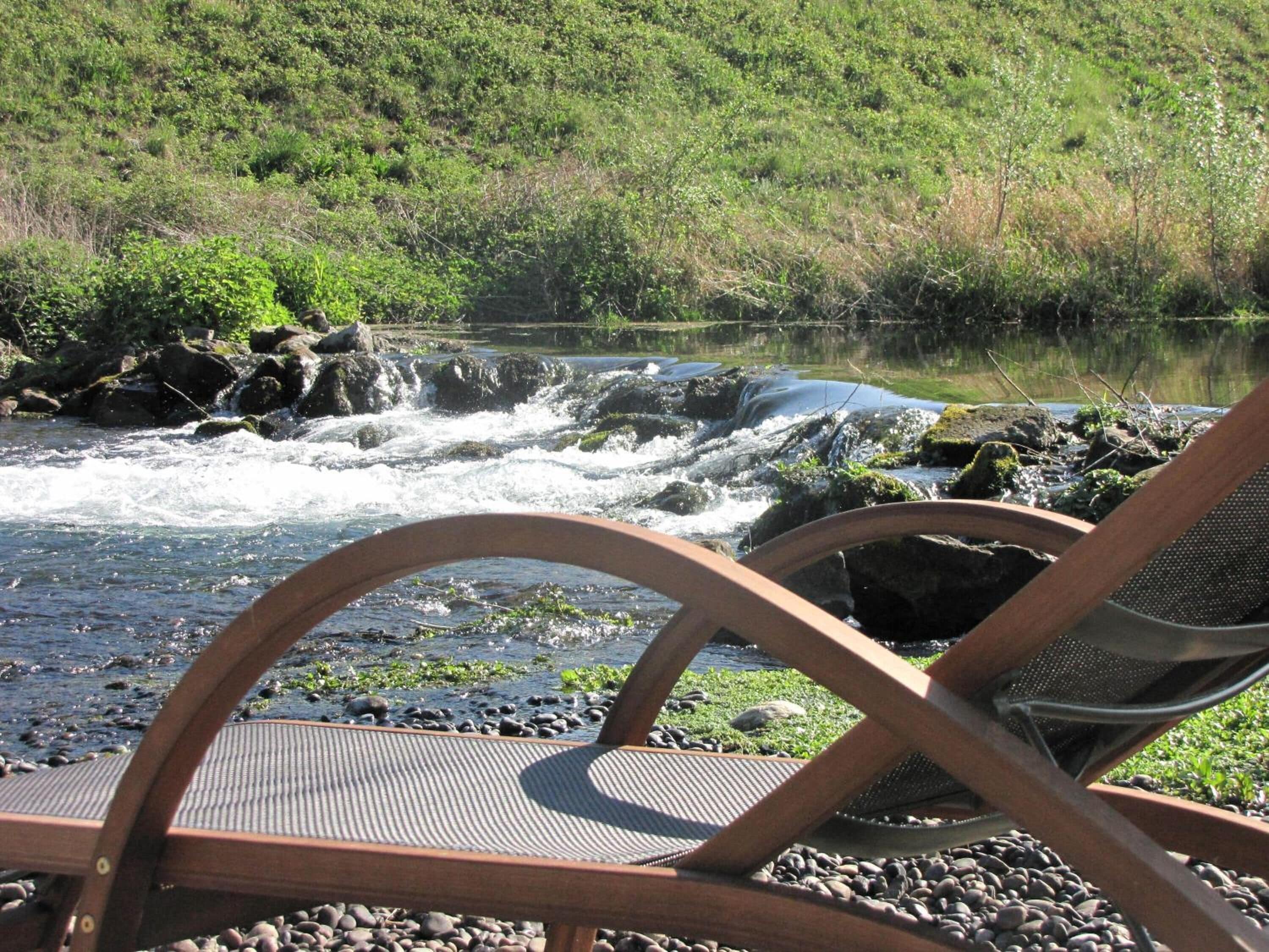 Ein Stuhl mit Blick auf einen Fluss, dessen Bett aus Felsen besteht, und einen bewaldeten Hügel.