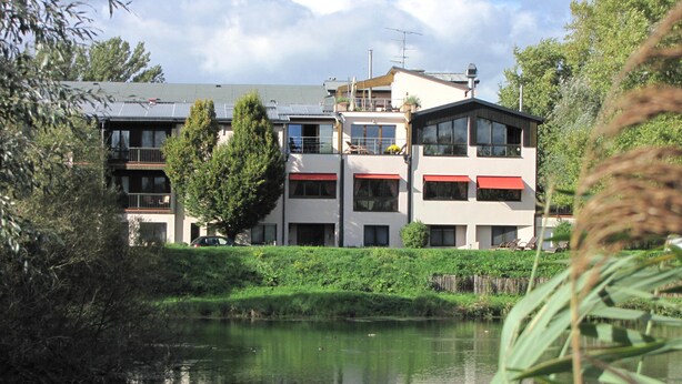 A modern building with multiple balconies and large windows, situated next to a calm body of water. - Hotel le Caballin (Vogelgrun)