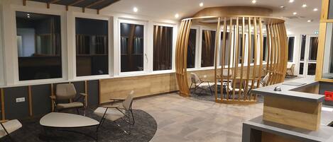 A modern hotel lobby with a reception desk, seating area, and large windows.