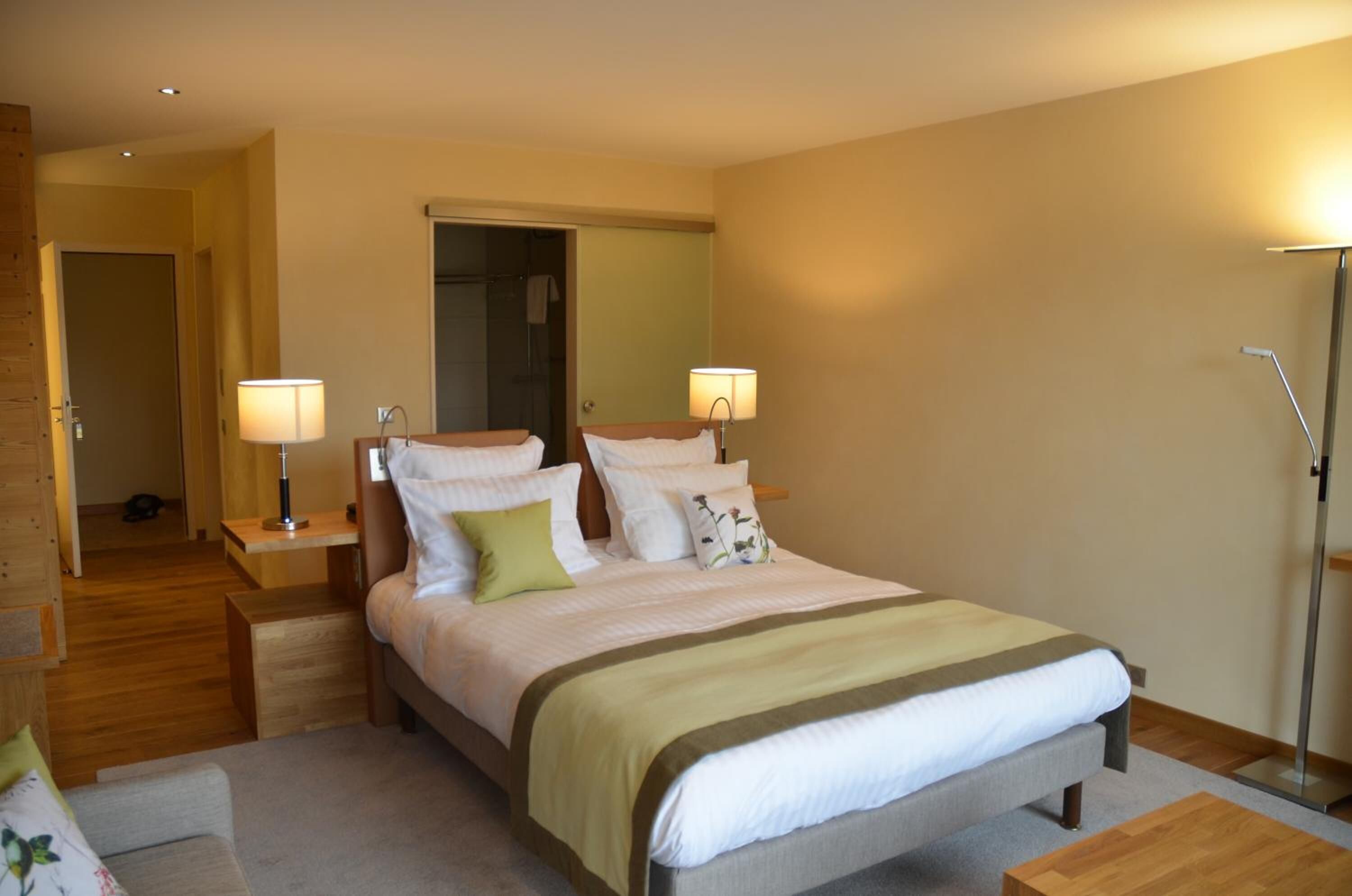A bedroom with a large bed, two bedside tables, a nightstand, a mirror, and a floor lamp.