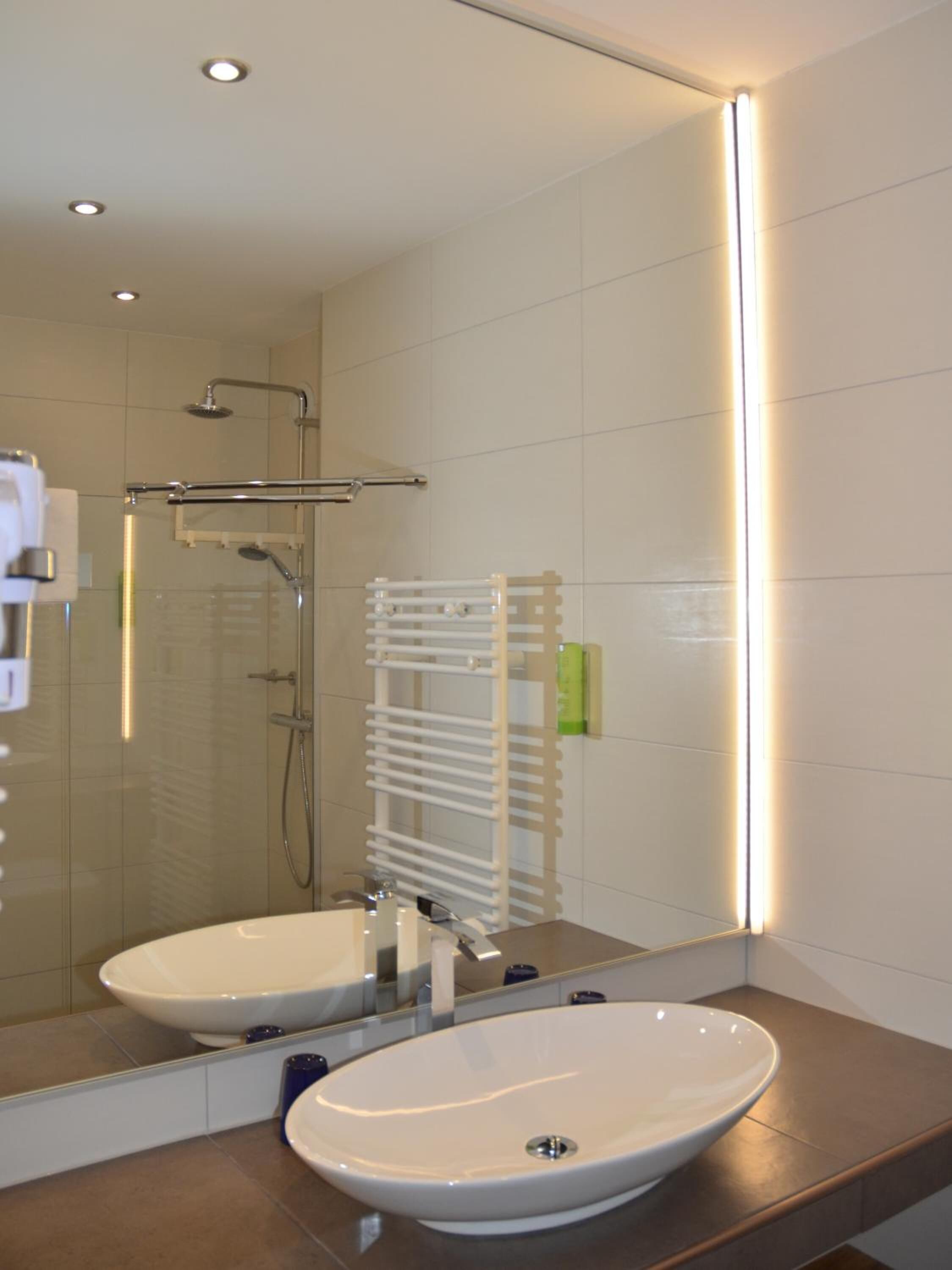 Un bagno moderno con uno specchio grande, due lavandini, una cabina doccia in vetro e un portasciugamani.