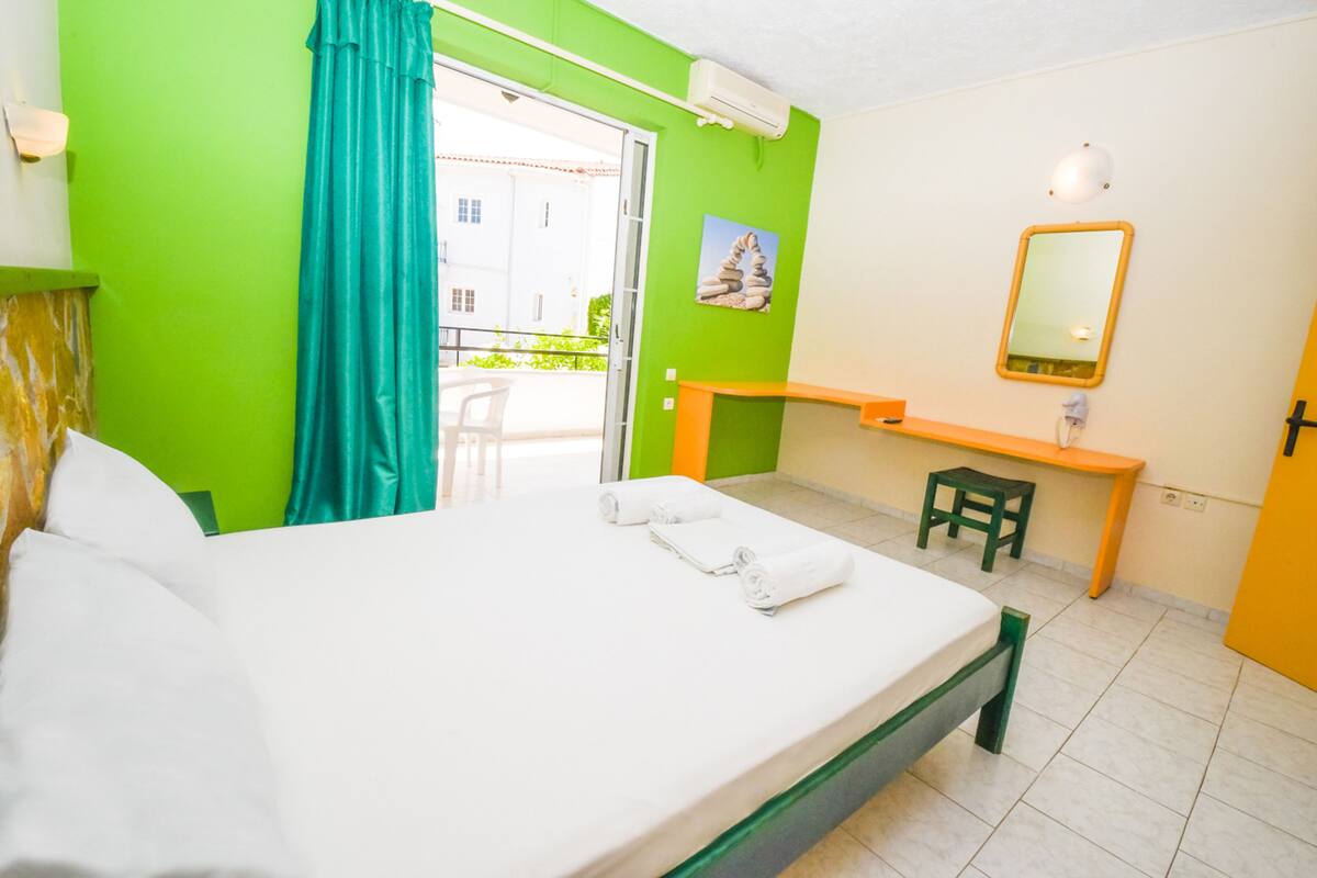 A hotel room with a bed, a desk, a chair, a mirror, and a window with curtains.