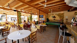 An outdoor cafe with wooden tables and chairs, a pool table, and a bar area. - Vanessa Hotel (Zakynthos)