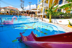 A swimming pool with a slide, surrounded by buildings with balconies and outdoor seating areas. - Vanessa Hotel (Zakynthos)