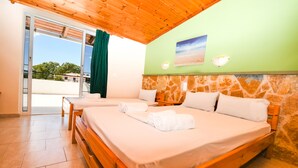 A room with two beds, wooden headboards, a stone wall, and a view through a glass door. - Vanessa Hotel (Zakynthos)